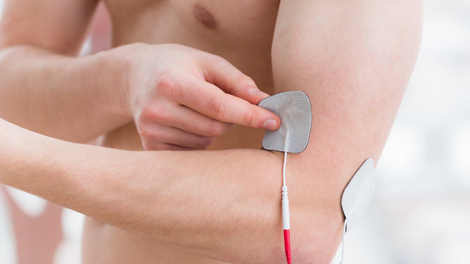 A person pressing a TENS electrode pad onto the upper arm